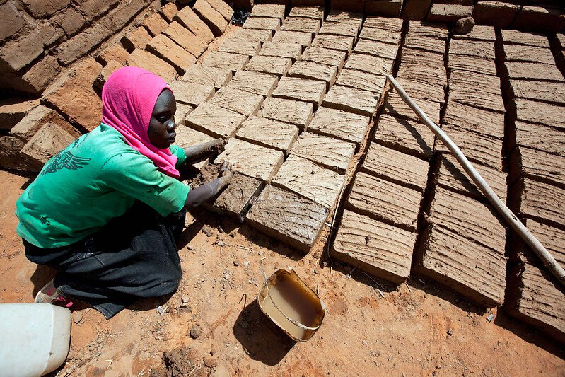 A disabled woman building her own house. Abu Shouk: Kaltoum Yakoub Issa, 19 years old, makes bricks for her new house in Abu Shouk camp for internally displaced people (IDP), in North Darfur. Kaltoum, originally from Jebel Seet (North Darfur), lost her left hand and part of the other was seriously bounded when her village was attacked and her house burnt ten years ago. It was when her family fled to Abu Shouk and was helped by International Rescue Committee (IRC) to get an artificial hand. However, during the last years, her parents moved away and she is now alone with one sister in the IDP camp, and struggling with her already useless prosthesis to build her own house. Photo by Albert Gonzalez Farran - UNAMID/flickr, CC BY-NC-ND 2.0<br>