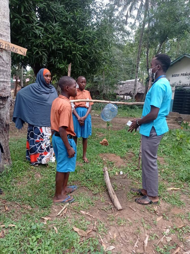 Student helps pupils to build a tippy tap installation for hand washing at the primary school in Bodoi. Photo: &copy; Rebekah Makau