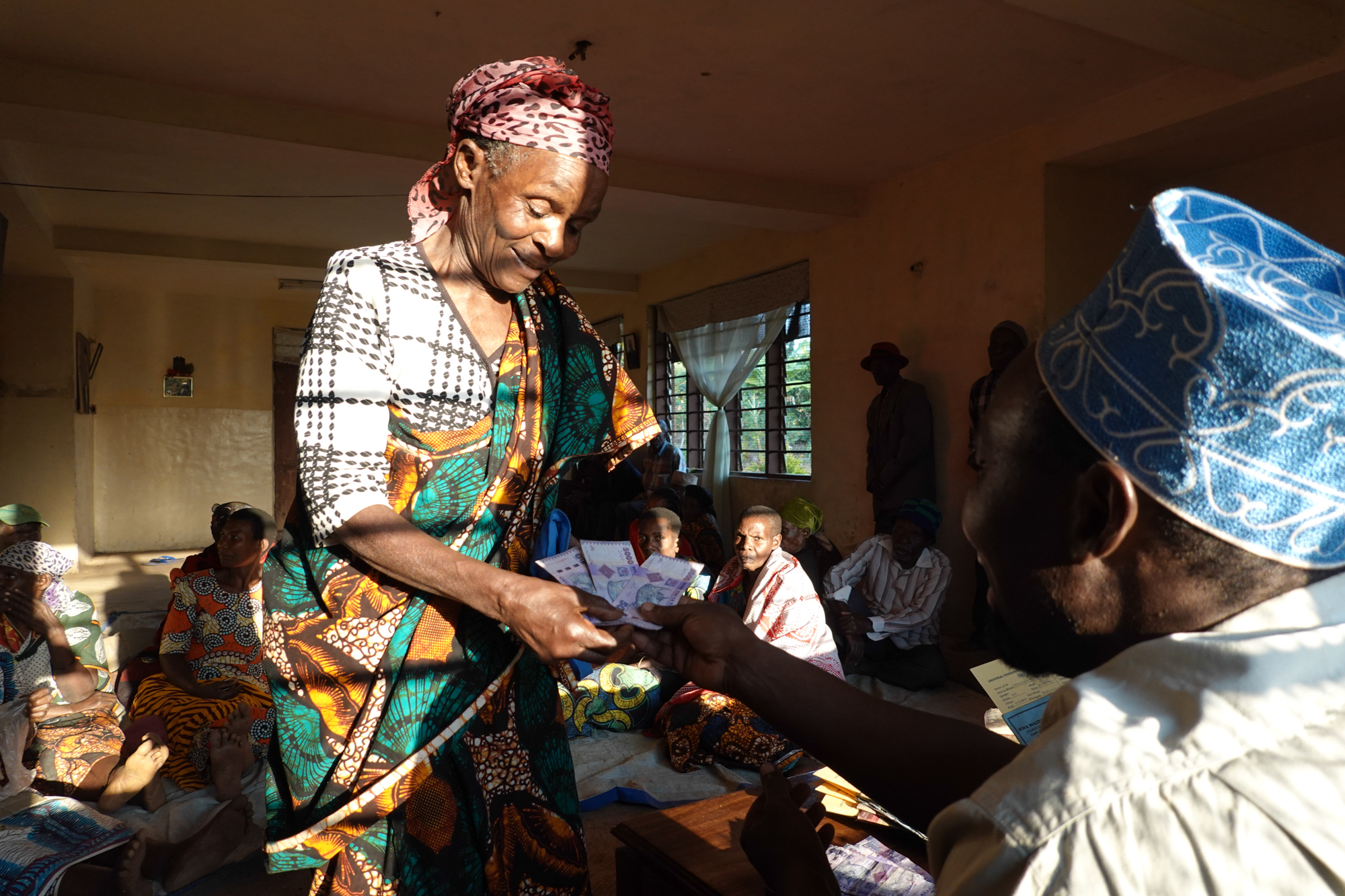 Gemeindebasiertes Rentenprogramm und Geldtransfers. Kwa Wazee hat ein gemeindebasiertes Rentenprogramm eingef&uuml;hrt, das &auml;ltere Menschen mit monatlichen Geldtransfers versorgt und damit einen wichtigen Beitrag zur Verringerung von Isolation und Einsamkeit leistet. Anstatt das Geld isoliert auszuh&auml;ndigen, organisiert Kwa Wazee pers&ouml;nliche Treffen, bei denen die &auml;lteren Menschen ihre Rente gemeinsam mit anderen erhalten. Diese Treffen f&ouml;rdern soziale Interaktionen, da die &auml;lteren Menschen &uuml;ber ihre finanziellen Ressourcen diskutieren, Investitionsideen austauschen und Freundschaften schliessen. Dieser Ansatz erm&ouml;glicht es &auml;lteren Menschen, sich sozial verbunden und wirtschaftlich gest&auml;rkt zu f&uuml;hlen, wodurch das Risiko der Einsamkeit verringert wird. Foto: &copy; Ren&eacute; Schraner, Verein Kwa Wazee